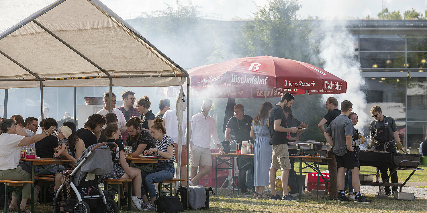 Bei einem Grillfest sitzen mehrere Menschen an einem Tisch. Andere stehen in der Schlange der Essensausgabe. Foto: Uwe Moosburger, altrofoto.de
