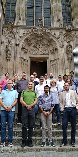 Personen stehen auf der Treppe vor einem Kircheneingang.