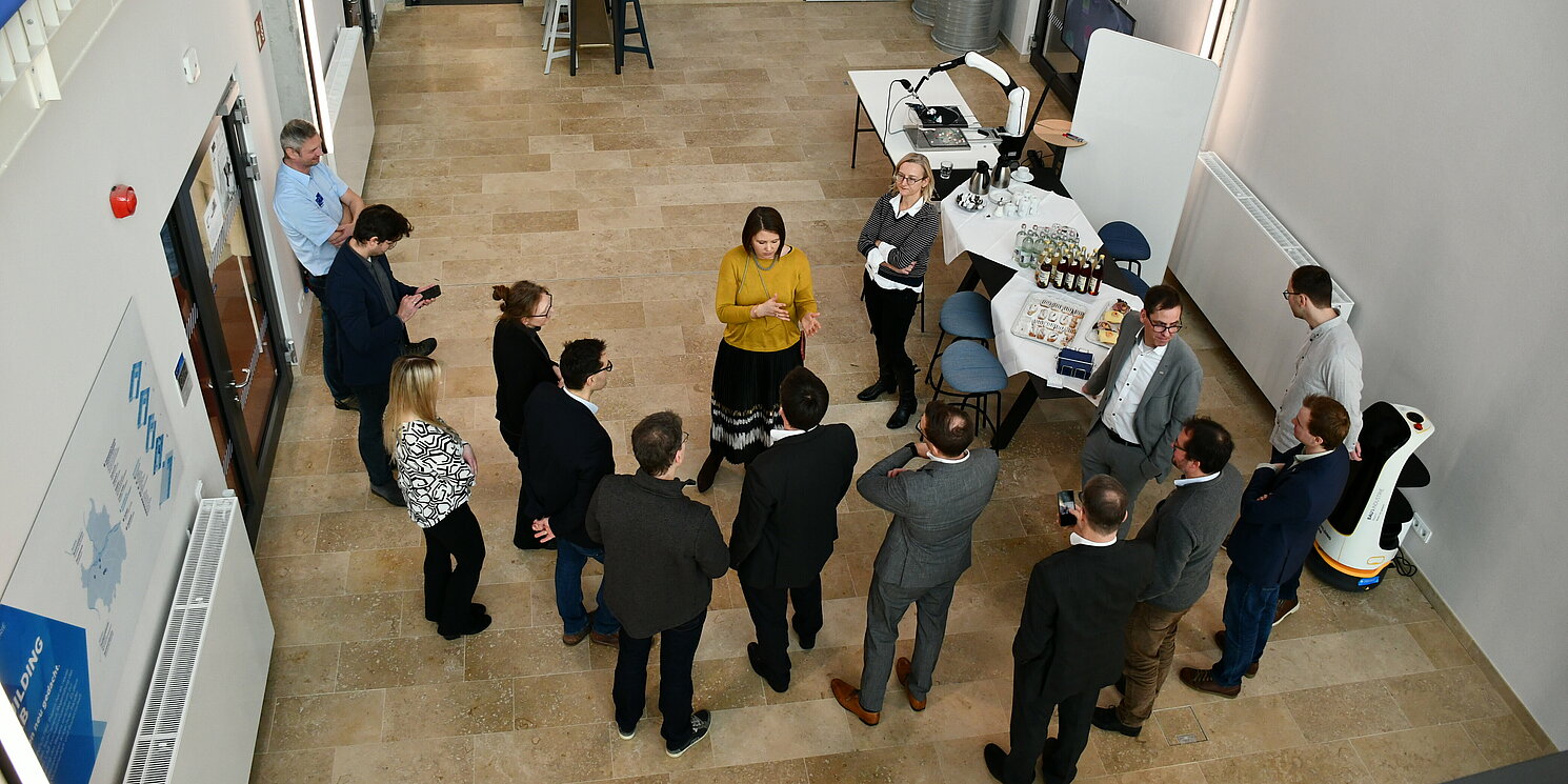 Bei einem Austausch mit den Wissenschaftlerinnen und Wissenschaftlern zeigte sich Dr. Carolin Wagner begeistert vom KI-Forschungsspektrum an der OTH Regensburg. Foto: OTH Regensburg/Simone Grebler Mehrere Personen unterhalten sich angeregt.