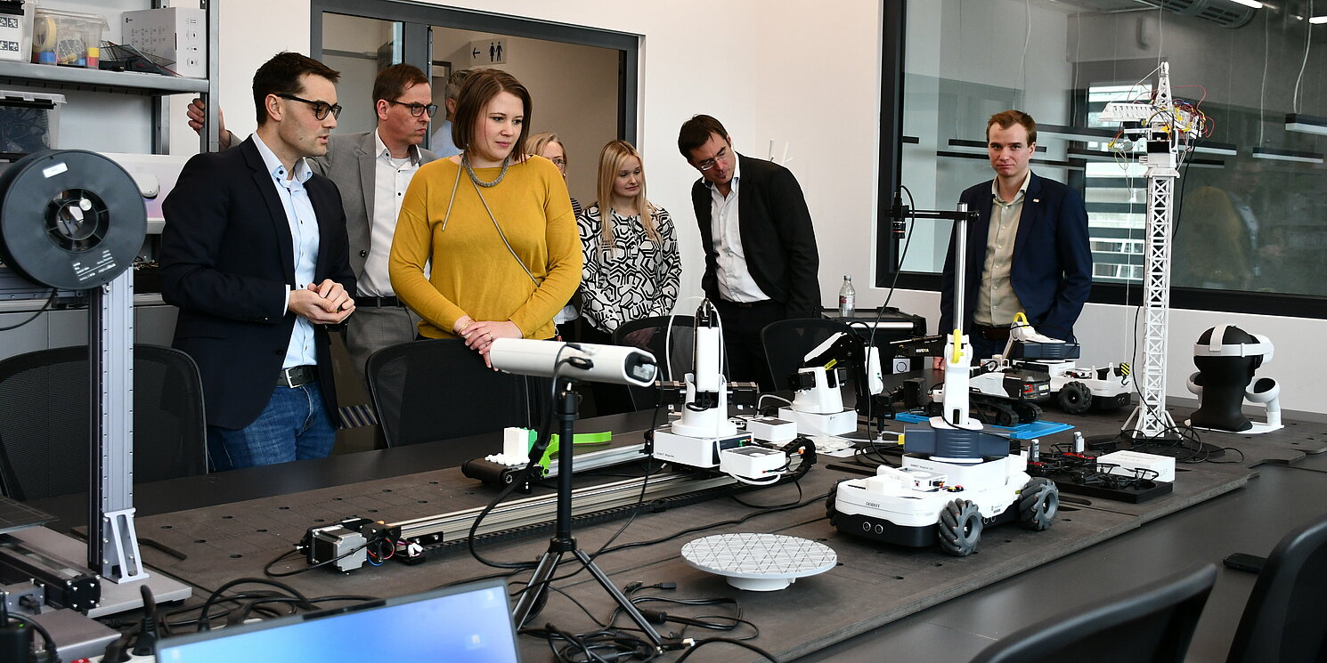 Prof. Dr. Mathias Obergrießer führte die Teilnehmenden durch das Building Lab und gab nähere Informationen zu der hochmodernen Ausstattung mit Roboterlaboren und Co-Working-Spaces. Foto: OTH Regensburg/Simone Grebler Mehrere Personen betrachten die moderne Ausstattung in einem Labor.